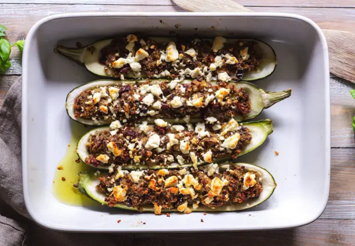 Fyra halverade zucchinis fyllda med en smakrik blandning och toppade med fetaost, redo att avnjutas som gratinerad zucchini.