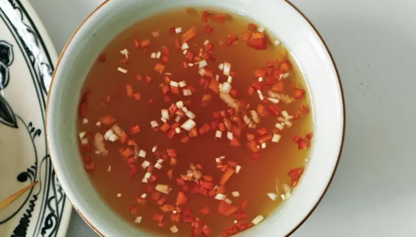 En skål med gyllene nuoc cham sås, toppad med finhackad röd chili och vitlök. En smakrik dipp som lyfter vilken rätt som helst.