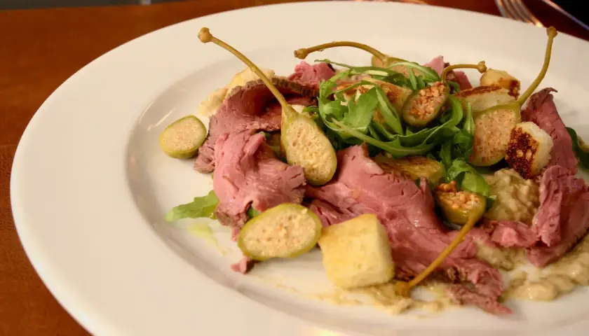 En tallrik med tunt skivad rostbiff, kapris, ruccola och krutonger. En klassisk vitello tonnato-inspirerad rätt.