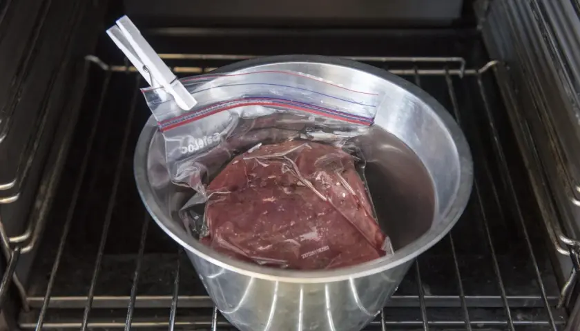 Rostbiff sous vide i en skål med vatten, klämd med en klädnypa, placerad på en ugnsgaller.