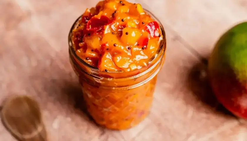 En burk med mango chutney, perfekt för ditt nästa chutney recept. En hel mango och en träsked syns också.