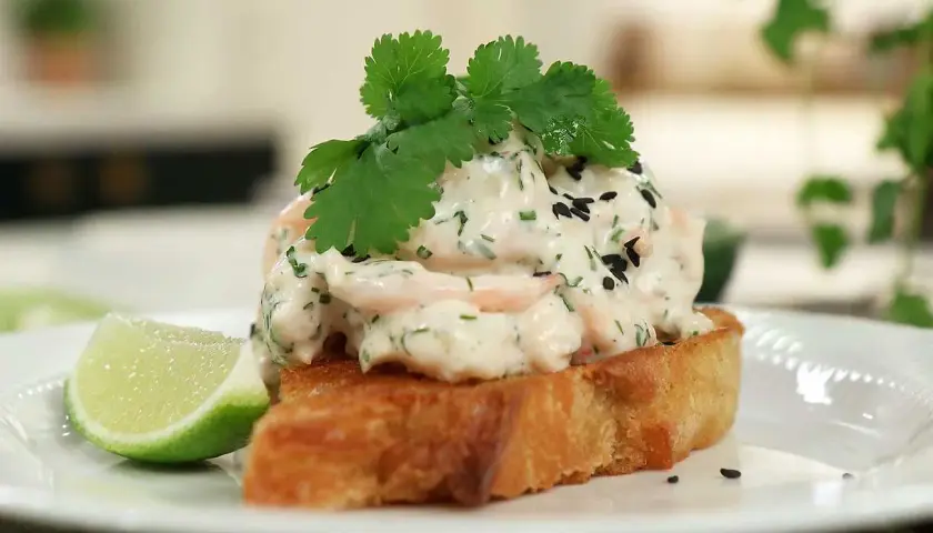 En rostad brödskiva toppad med krämig skagenröra, färska örter, svarta sesamfrön och en limeklyfta. En spännande asiatisk skagen-twist.