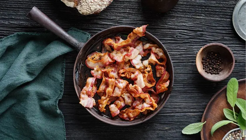 Knaperstekt bacon i panna, redo att avnjutas med nybakat bröd och färska örter.