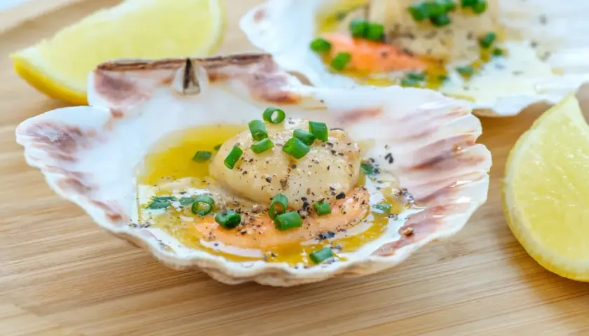 Läckra pilgrimsmusslor i skal, serverade med smält smör, örter och citron. Ett perfekt pilgrimsmusslor recept för en festmåltid.