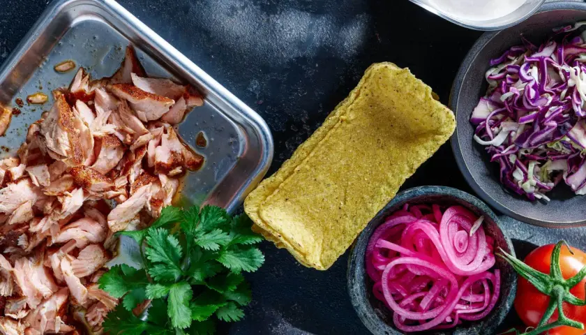 Förberedelser för lax tacos: saftig lax, majstortillas, rödlök, rödkål, koriander och tomater.