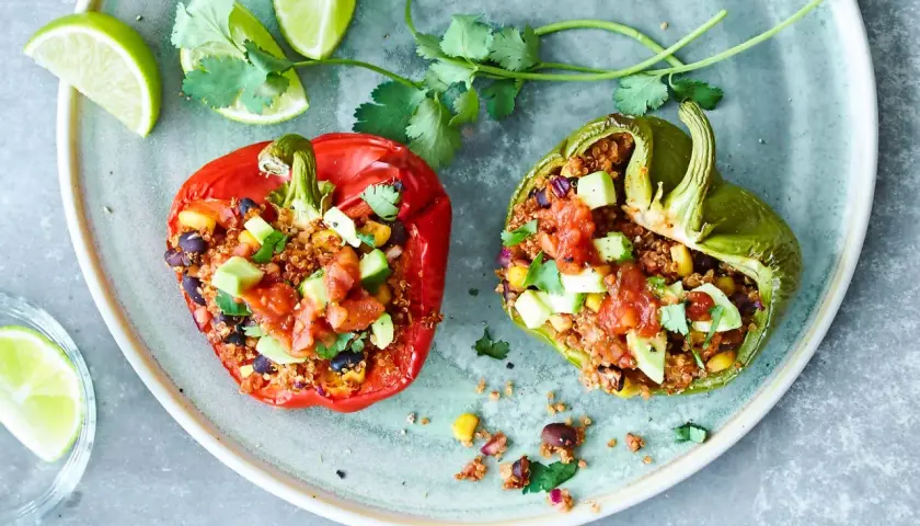 Två färgglada, fyllda paprikor med quinoa, svarta bönor och majs, toppade med salsa och avokado. Serveras med limeklyftor och koriander.