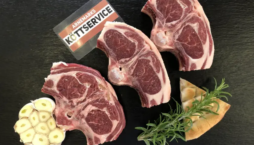 Tre saftiga lammkotletter, vitlök och rosmarin ligger redo för att grilla lammkotletter. En bit focaccia ligger bredvid.