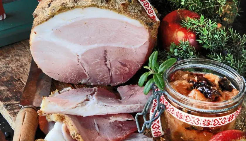 En saftig griljerad skinka i ugn, skuren i skivor, serveras med äppelchutney, en röd äpple och enbärskvist.