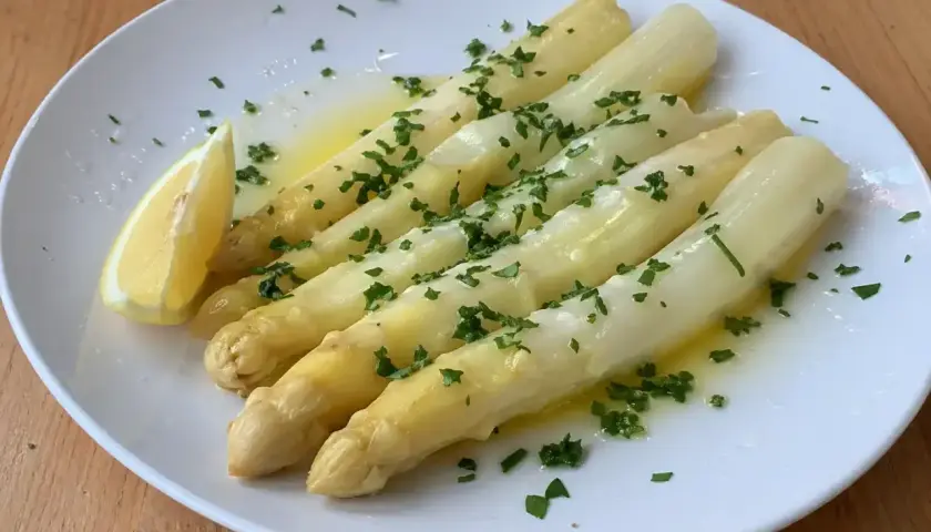 En tallrik med ångad vit sparris, garnerad med hackad persilja och en citronklyfta. En klassisk och delikat rätt.