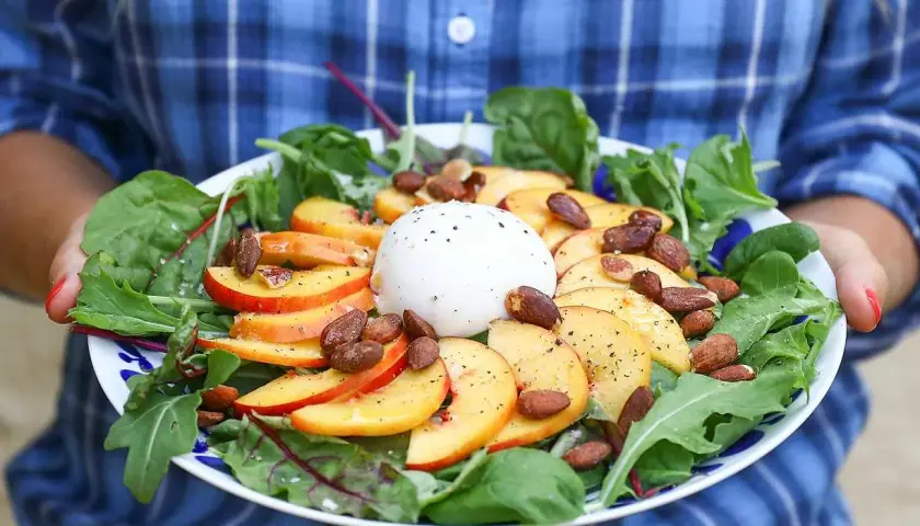 En somrig sallad med skivad persika, krämig burrata, mandlar och gröna blad. En perfekt kombination av sött och salt.
