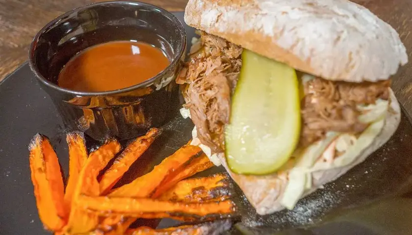 En saftig pulled pork-macka med krispiga sötpotatispommes och en skål med härlig sås till pulled pork.