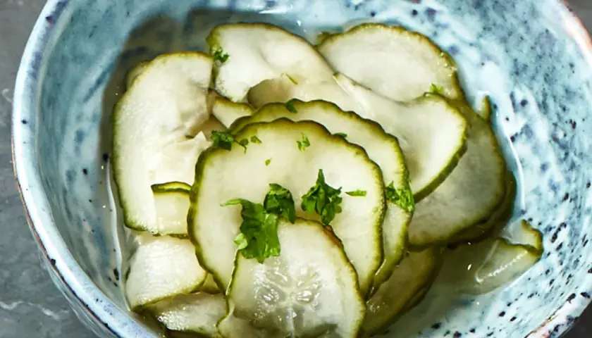 Skivade pressgurkor i en blå skål, toppade med färsk persilja. Ett enkelt och gott pressgurka recept.