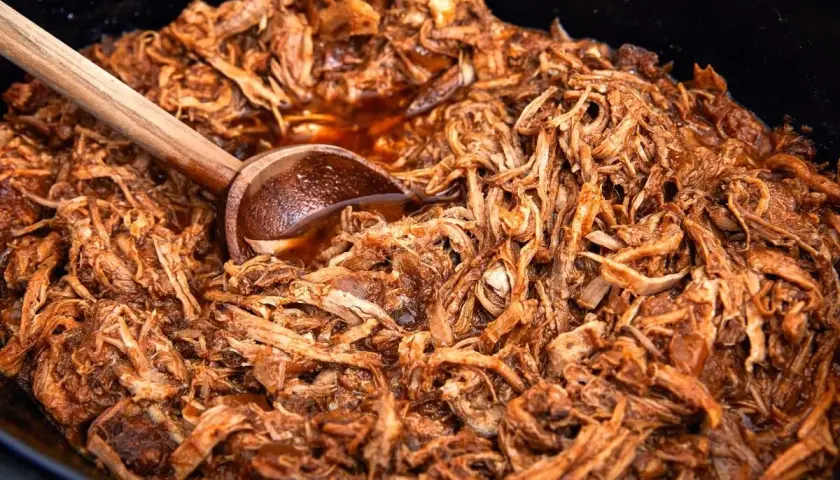 Saftigt pulled pork i en gryta, perfekt för ett gott recept. En träsked ligger i köttet.