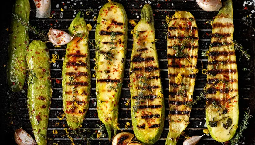 Grillad zucchini med vitlök, örter och citronzest på en grillpanna. Perfekt tillbehör för sommaren.