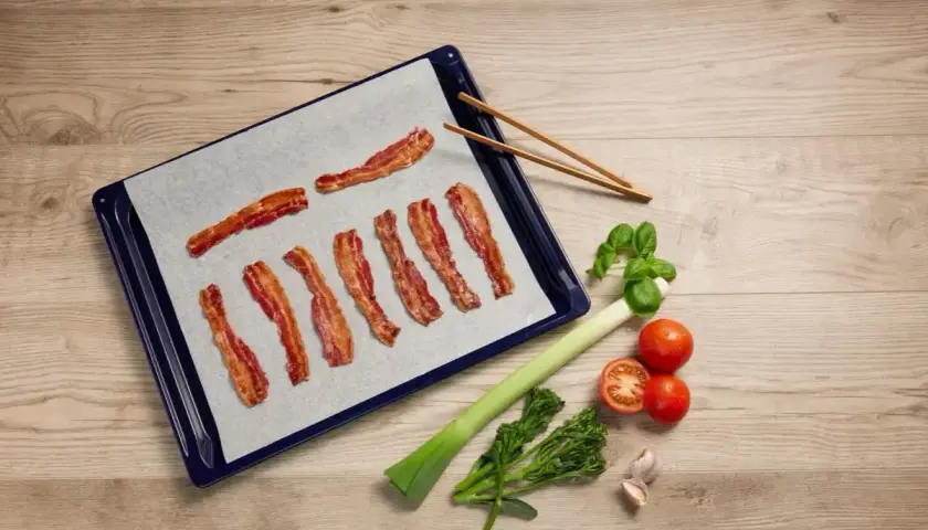 Bacon i ugn på bakplåtspapper, redo att serveras med färska grönsaker.