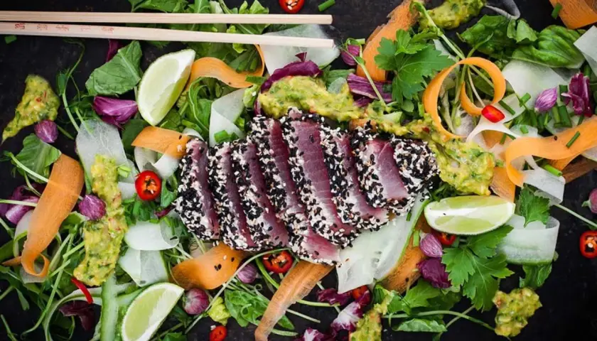 Halstrad tonfisk med sesamfrön, serverad med en fräsch sallad av grönsaker, lime och avokado. Ett perfekt halstrad tonfisk recept för en lätt lunch.