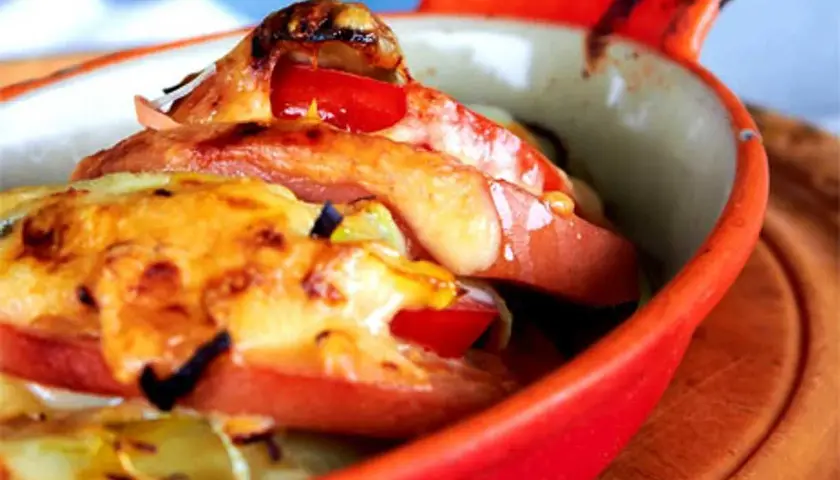 Baked falukorv with melted cheese and tomatoes in a red dish.