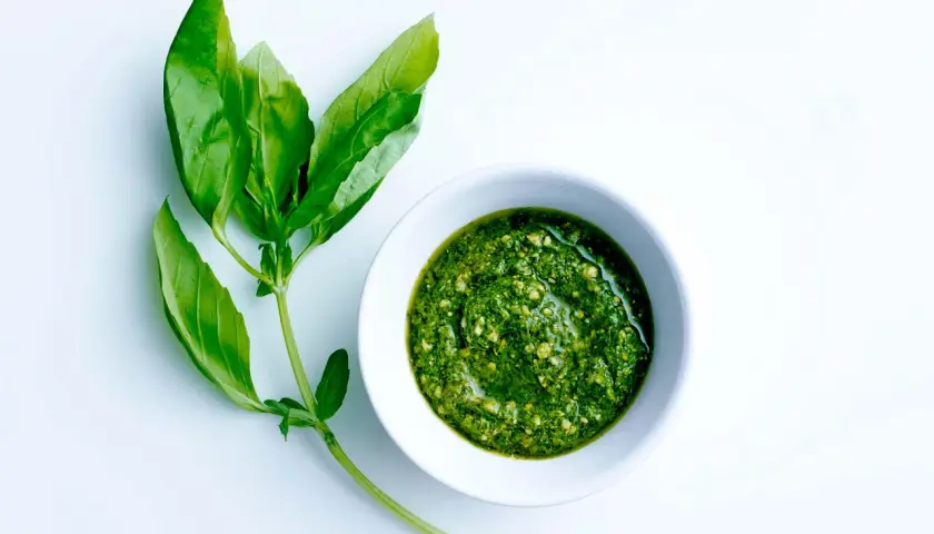 En skål med hemgjord egen pesto bredvid färska basilikablad.