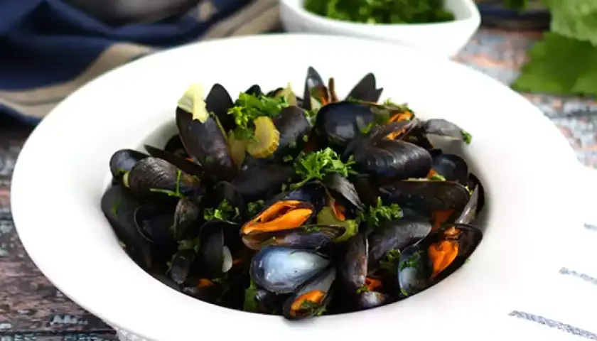 En skål med ångade musslor, moules marinières, garnerade med färsk persilja och serverade med en sidokål.