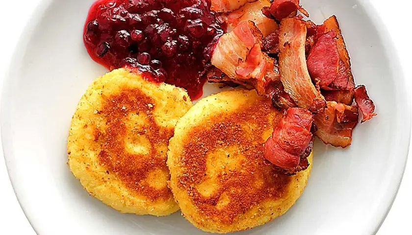 Två gyllene potatisbullar airfryer serveras med rårörda lingon och knaperstekt bacon.
