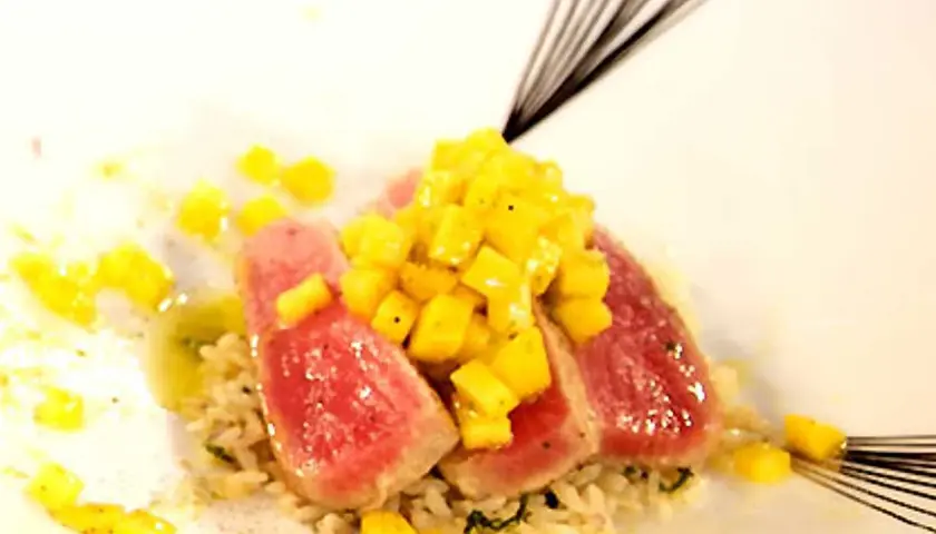 Röda skivor av tonfisk med tärnad mango ovanpå, serverade på ris. En utsökt kombination av tonfisk och mango.