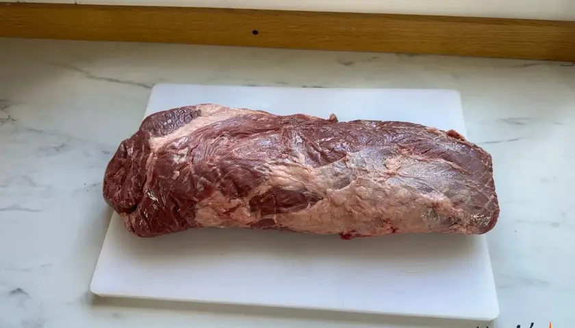 En rå, marmorerad brisket svenska ligger på en vit skärbräda.