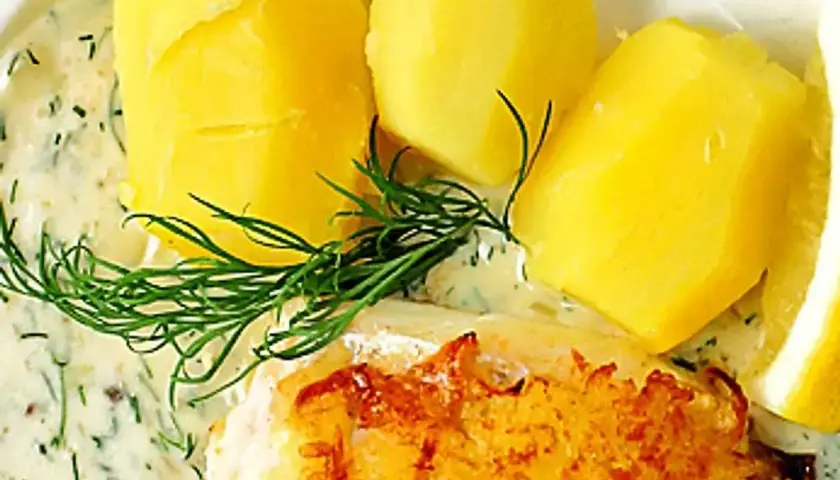 En portion med kokt potatis, en bit stekt fisk och en generös klick varm dillsås. Garnerat med färsk dill och en citronskiva.