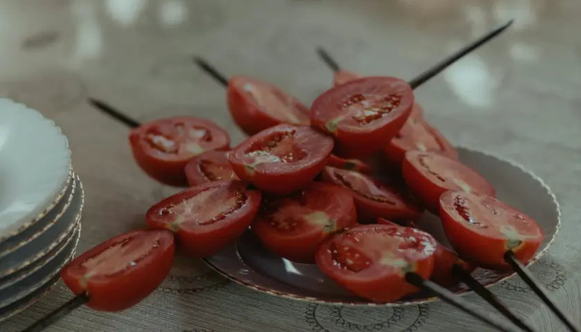 Halverade tomater på spett, redo för grillen. En stapel tallrikar syns till vänster.