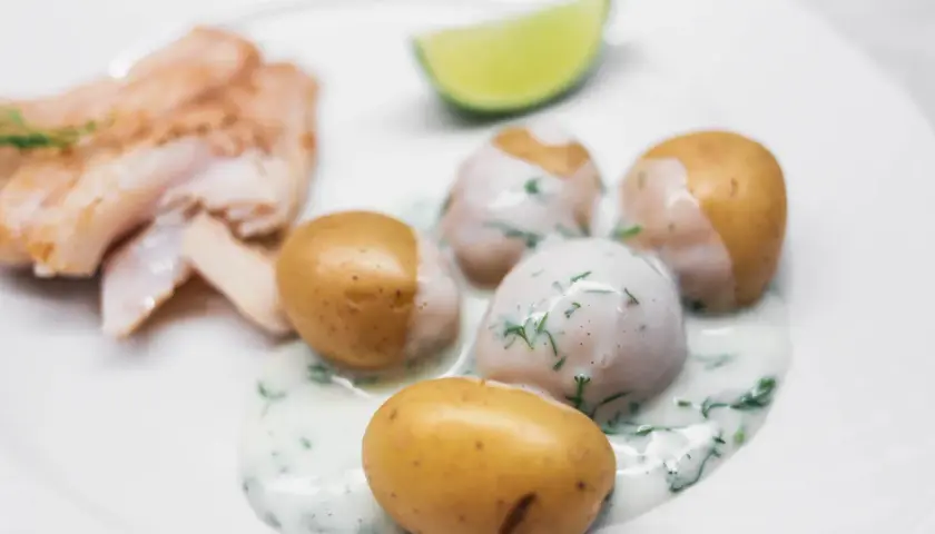 En tallrik med stuvad potatis, fisk och en limeklyfta. Potatisen är krämig och toppad med dill.