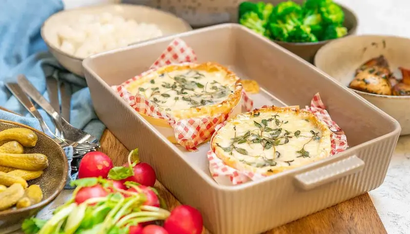 Två runda camembertostar i ugn, toppade med örter, serveras med rädisor, cornichoner och broccoli.