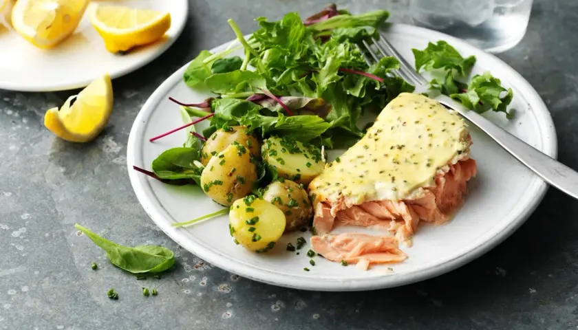En tallrik med pulled lax, potatis och sallad. En citronskiva ligger bredvid.