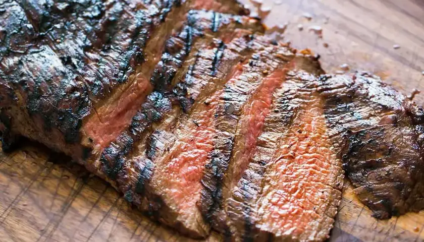 Skivad, grillad flankstek med vackra grillränder och en härlig röd kärna, redo att serveras med chimichurri.