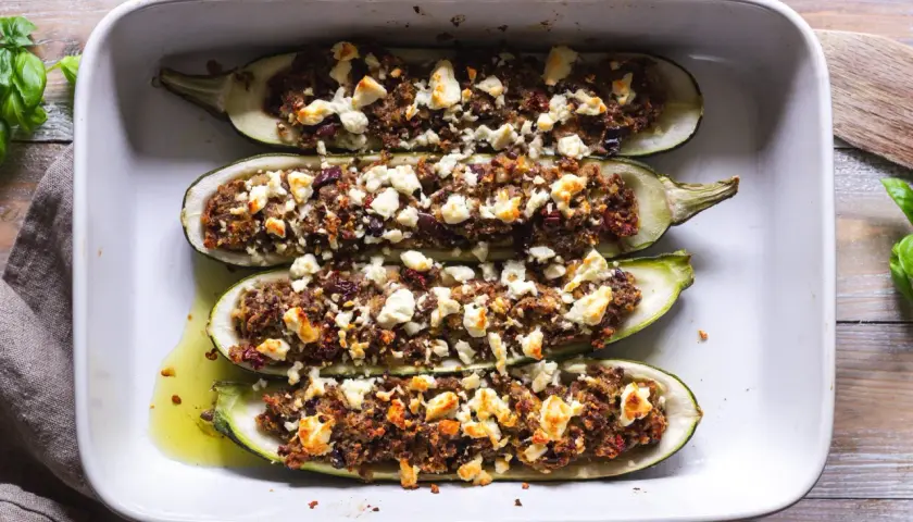 Fyra halverade zucchinis fyllda med en smakrik blandning och toppade med fetaost, redo att avnjutas som gratinerad zucchini.