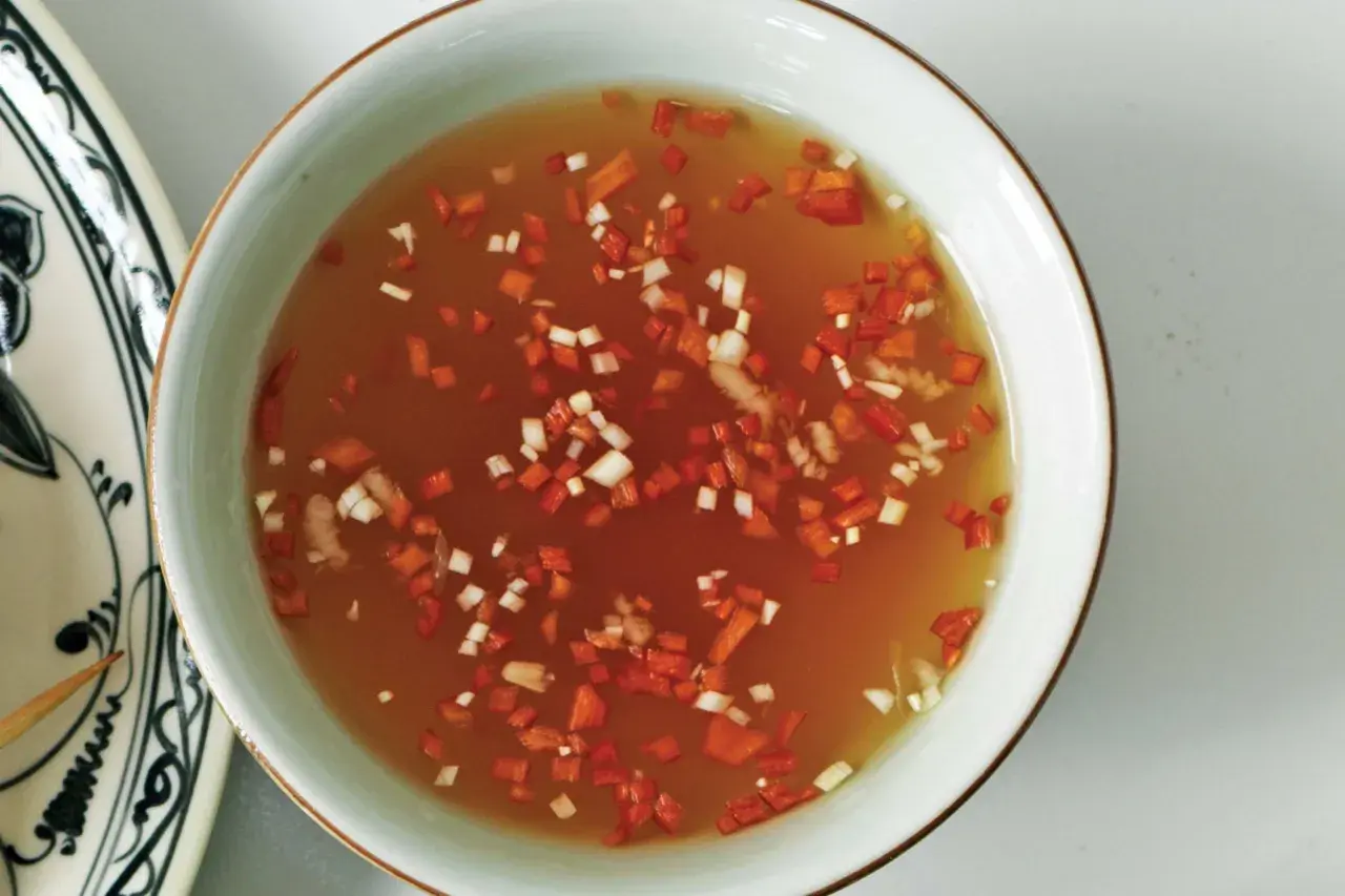 En skål med gyllene nuoc cham sås, toppad med finhackad röd chili och vitlök. En smakrik dipp som lyfter vilken rätt som helst.