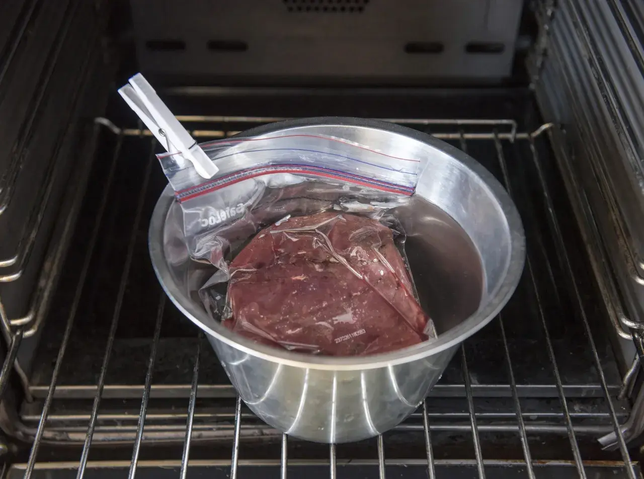 Rostbiff sous vide i en skål med vatten, klämd med en klädnypa, placerad på en ugnsgaller.