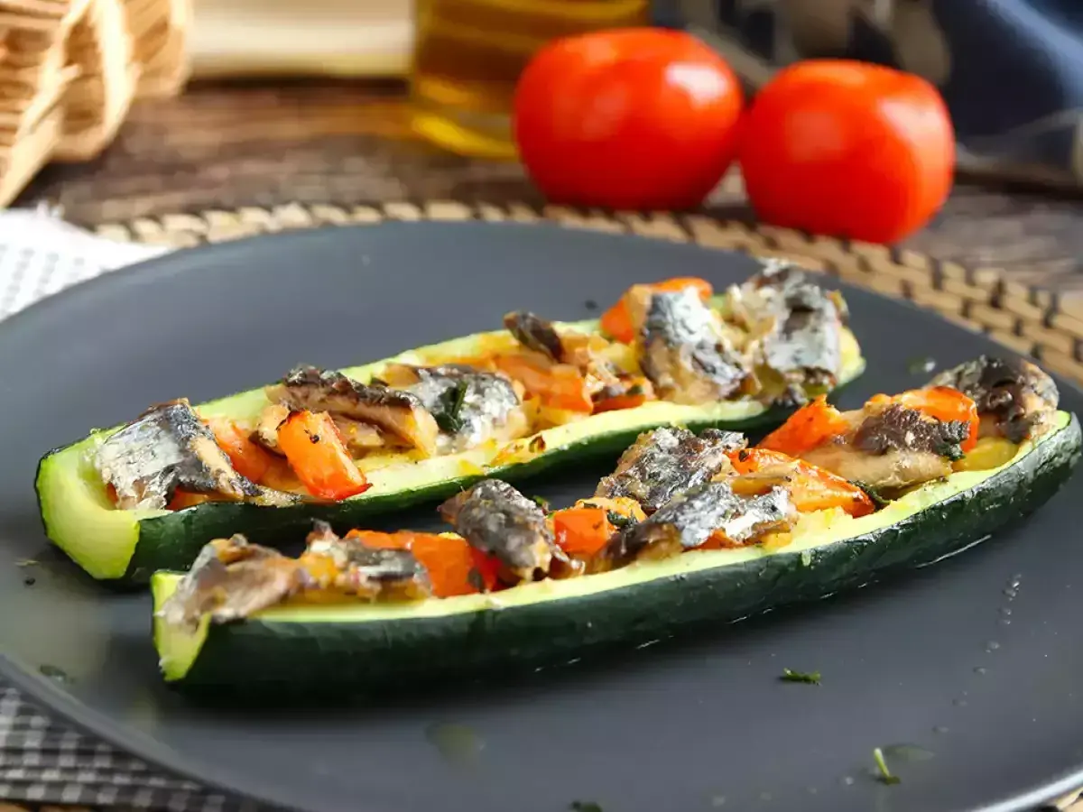 Två halvor av fylld zucchini med fisk och grönsaker på en mörk tallrik.