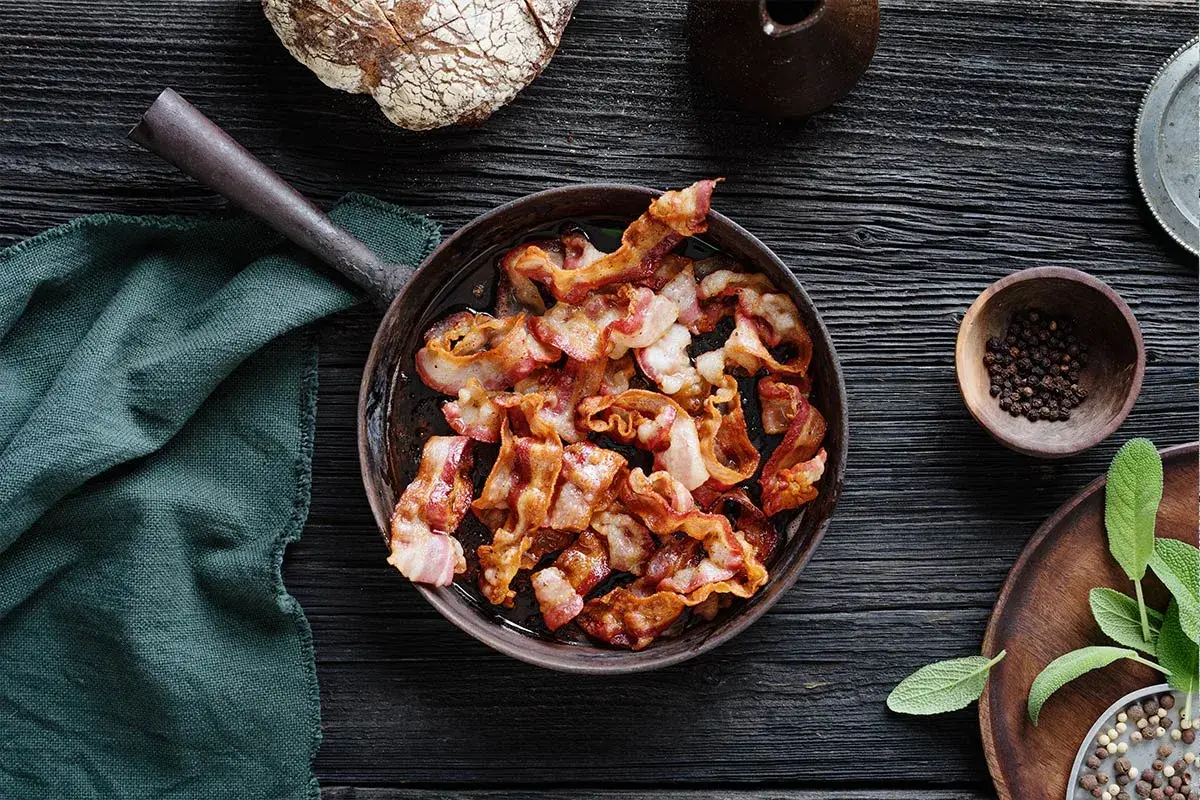 Knaperstekt bacon i panna, redo att avnjutas med nybakat bröd och färska örter.