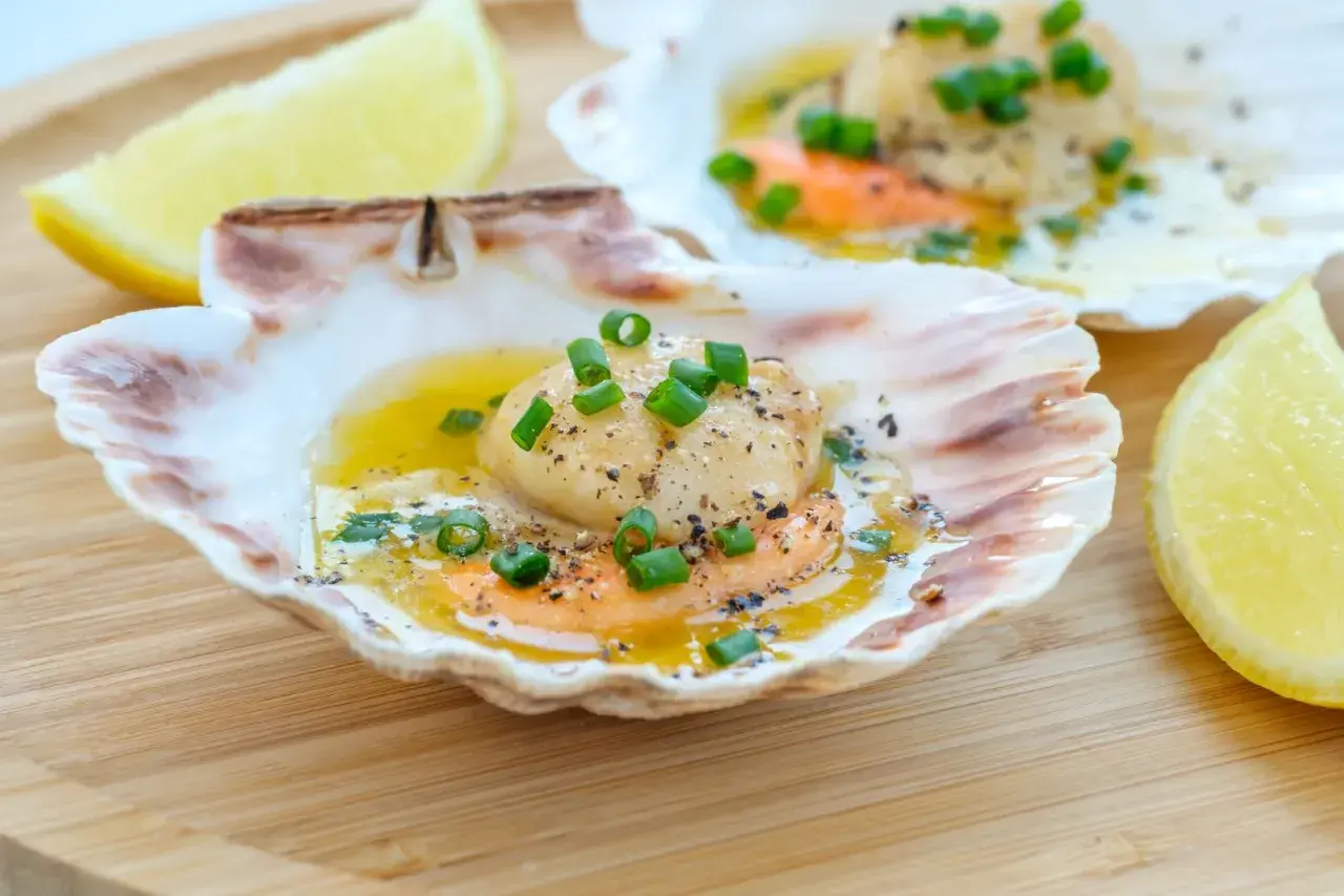 Läckra pilgrimsmusslor i skal, serverade med smält smör, örter och citron. Ett perfekt pilgrimsmusslor recept för en festmåltid.