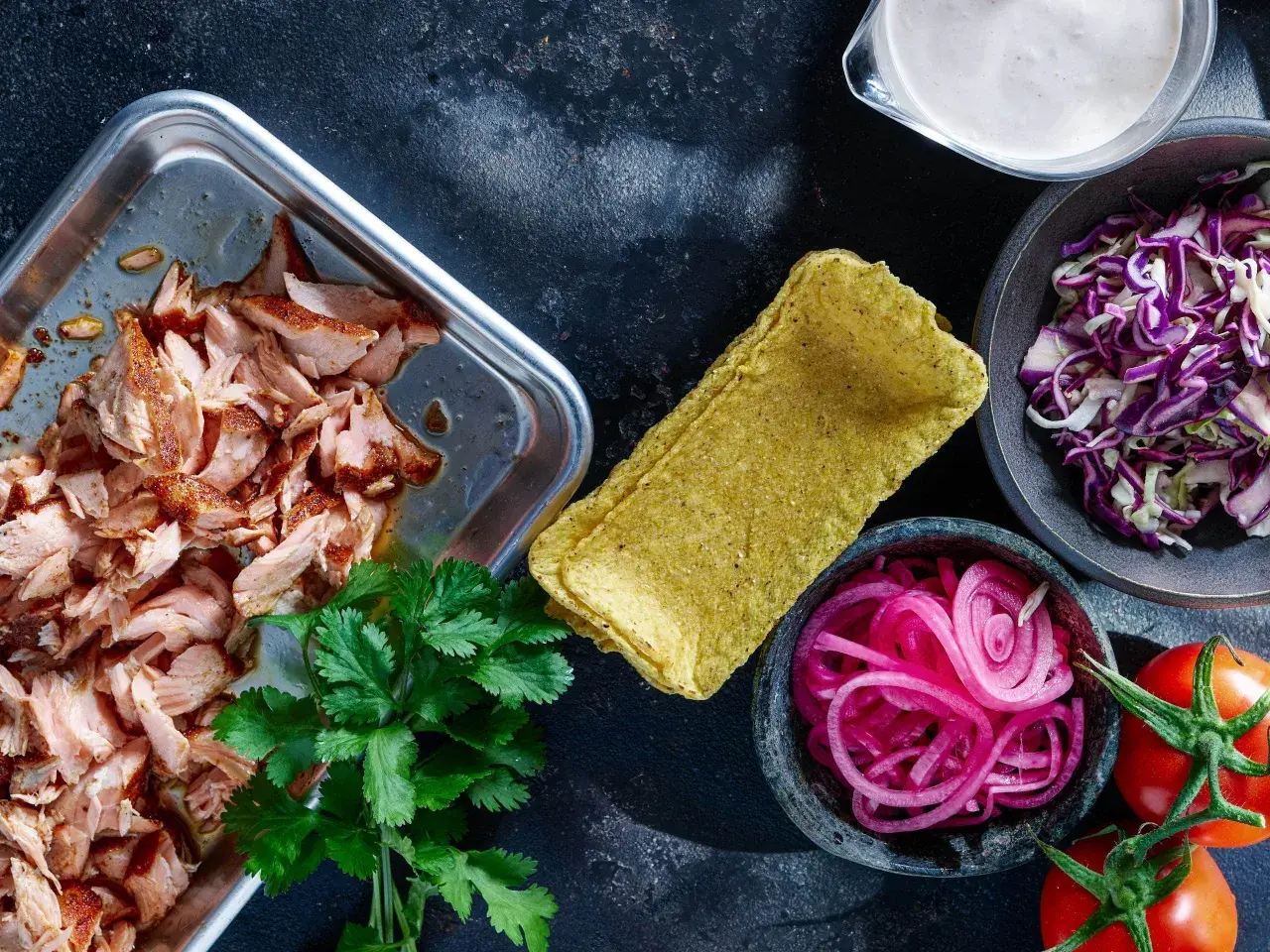 Förberedelser för lax tacos: saftig lax, majstortillas, rödlök, rödkål, koriander och tomater.