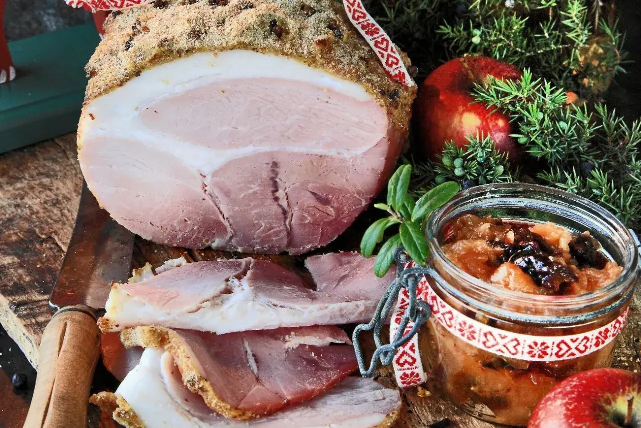 En saftig griljerad skinka i ugn, skuren i skivor, serveras med äppelchutney, en röd äpple och enbärskvist.