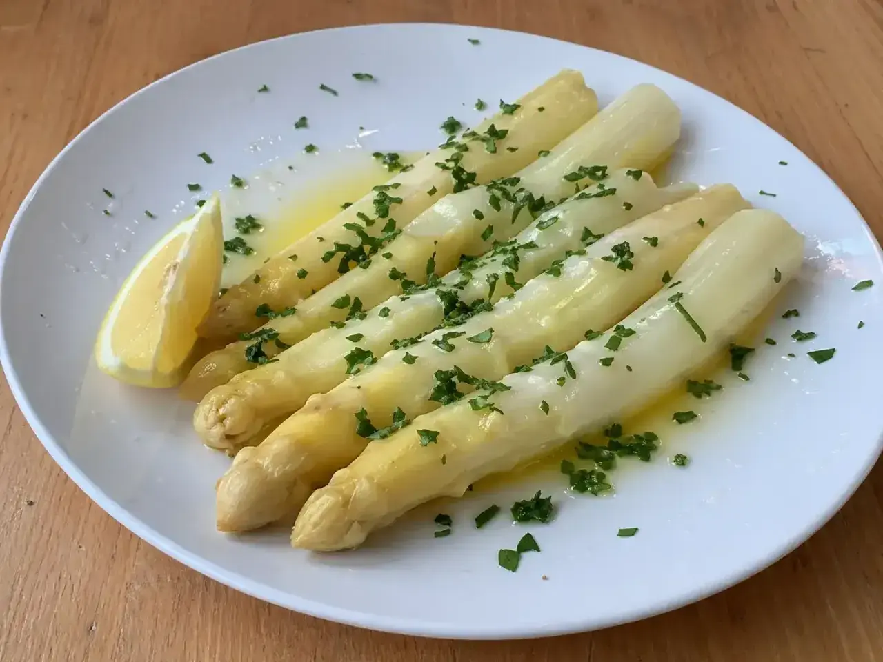 En tallrik med ångad vit sparris, garnerad med hackad persilja och en citronklyfta. En klassisk och delikat rätt.