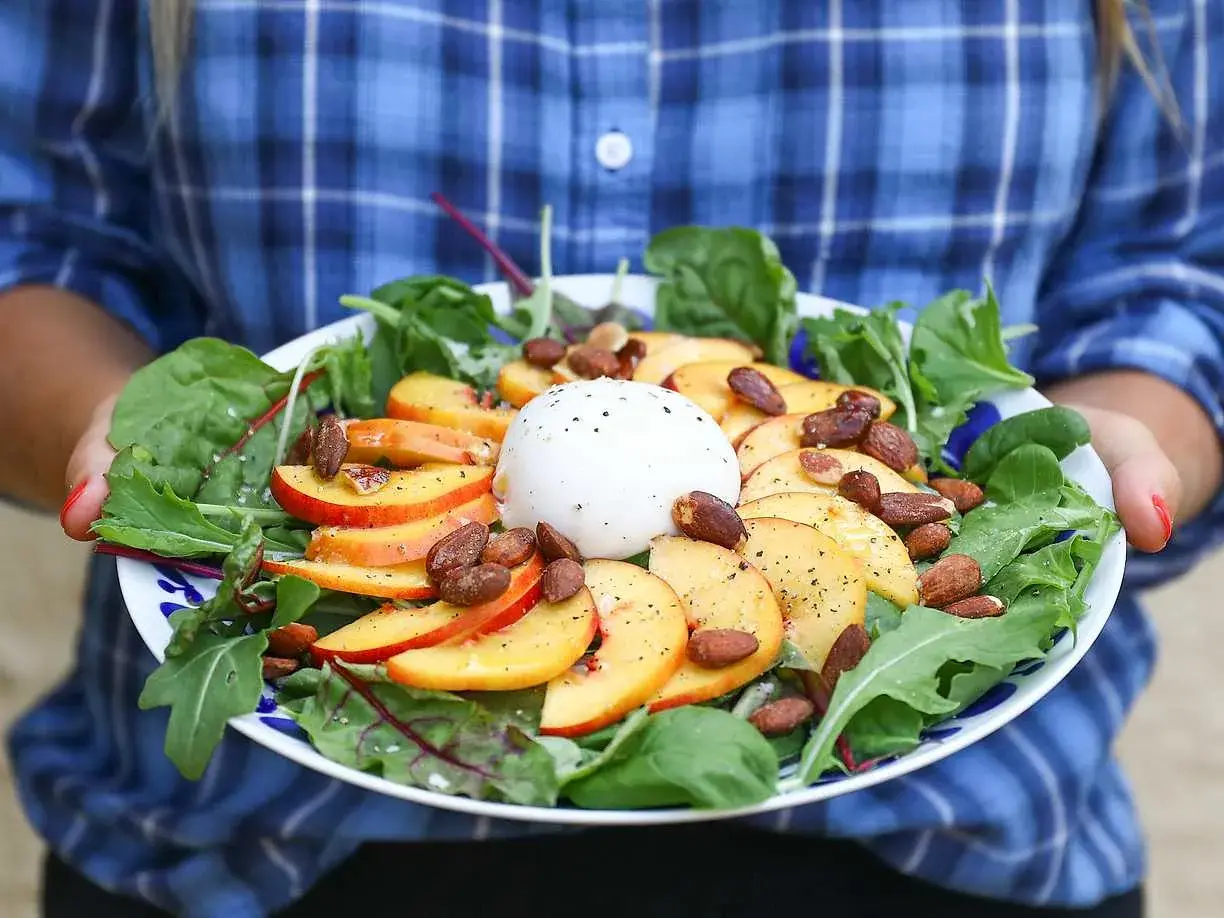En somrig sallad med skivad persika, krämig burrata, mandlar och gröna blad. En perfekt kombination av sött och salt.