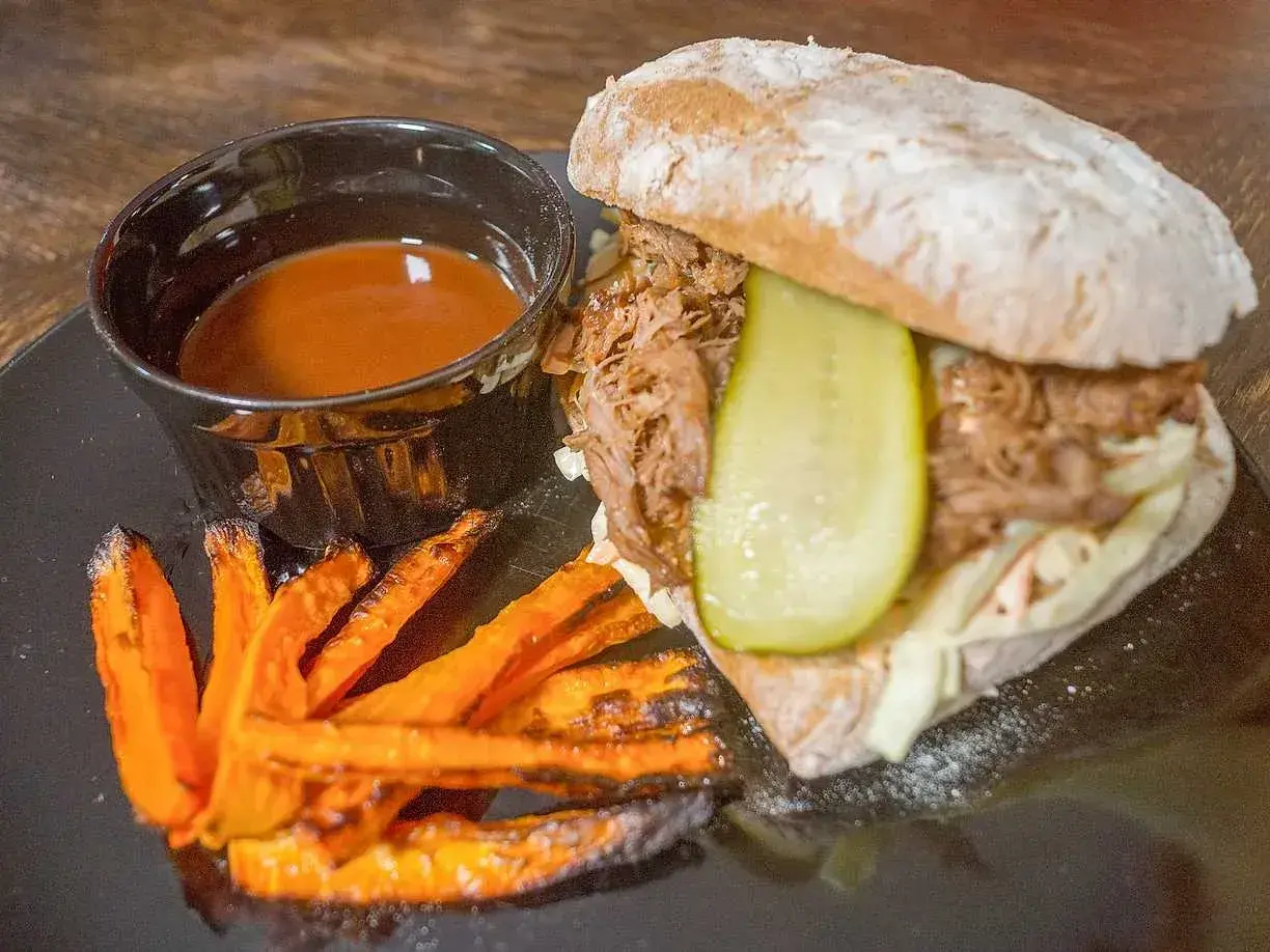 En saftig pulled pork-macka med krispiga sötpotatispommes och en skål med härlig sås till pulled pork.