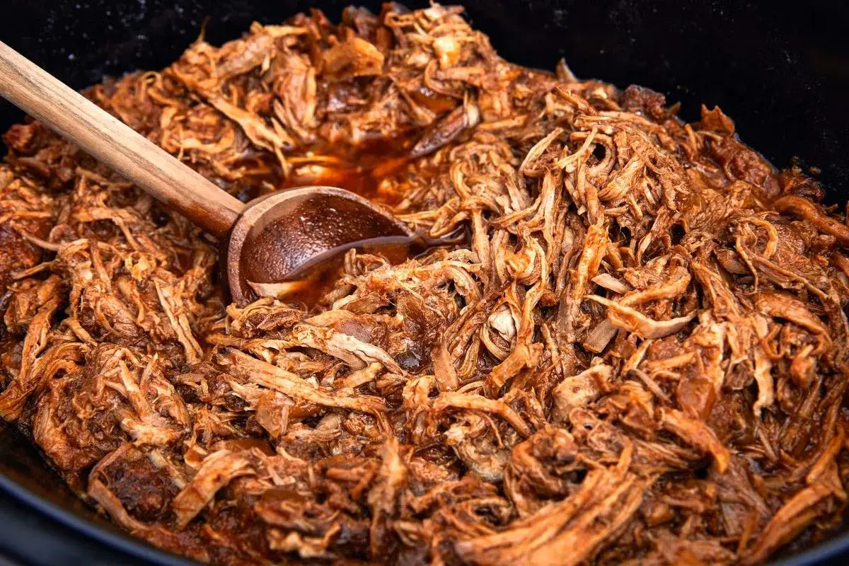 Saftigt pulled pork i en gryta, perfekt för ett gott recept. En träsked ligger i köttet.