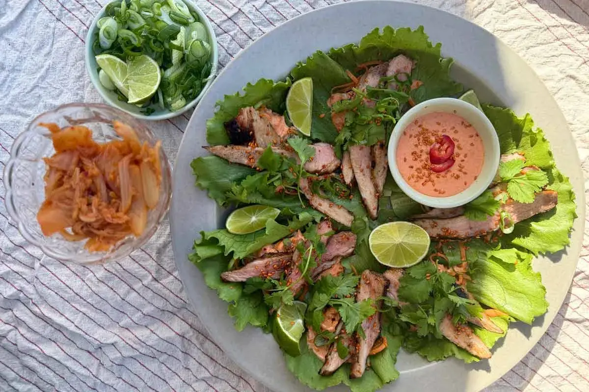 Grillad fläskkarré i salladsblad med kimchi, lime och en krämig sås. Ett perfekt pluma recept för en lätt och smakrik måltid.