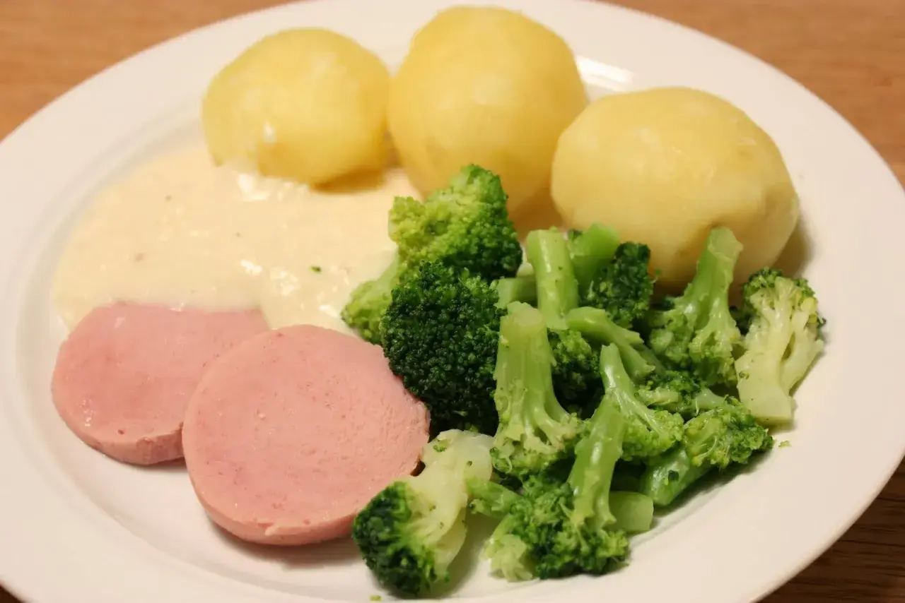 En tallrik med kokt falukorv med pepparrotssås, potatis och broccoli. En klassisk svensk middag.