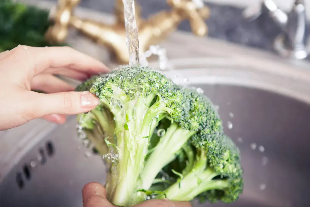 Färska broccolibuketter sköljs under rinnande vatten, redo för ett hälsosamt broccoli recept.