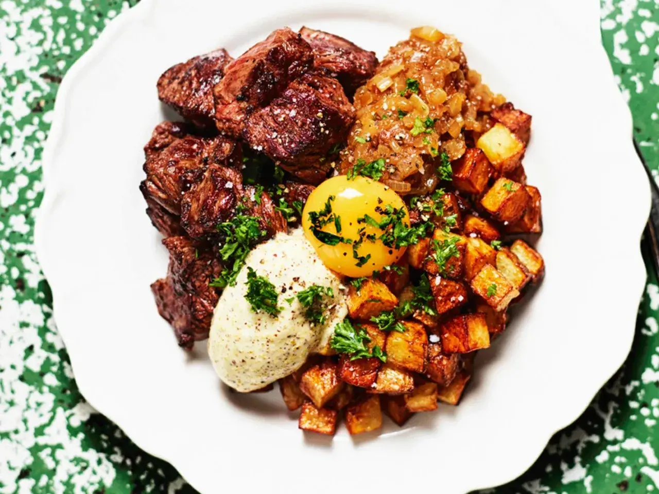 En tallrik med saftig biff, krispiga potatisbitar, en äggula och en klick sås. Ett spännande njurtapp recept att prova!