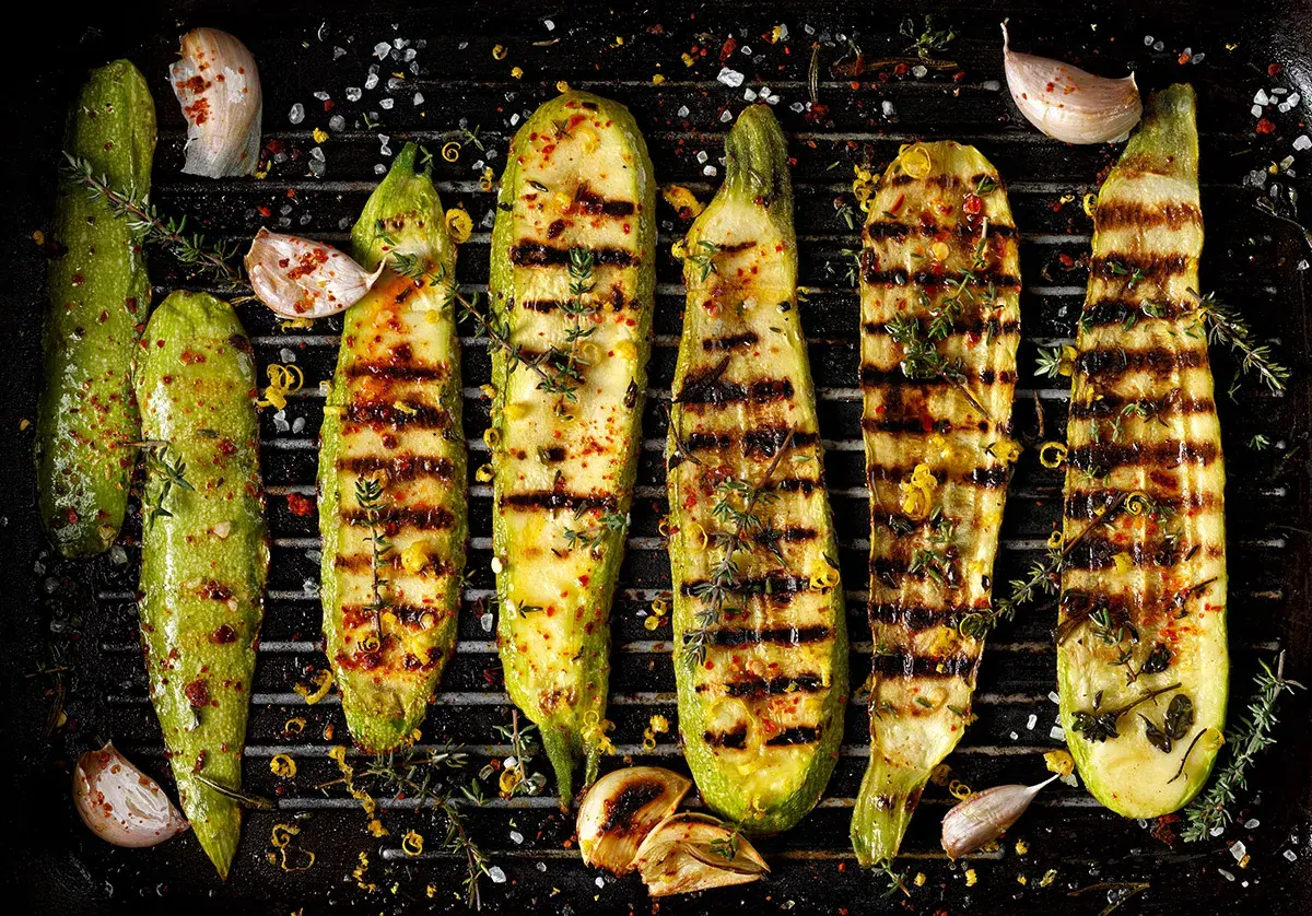 Grillad zucchini med vitlök, örter och citronzest på en grillpanna. Perfekt tillbehör för sommaren.
