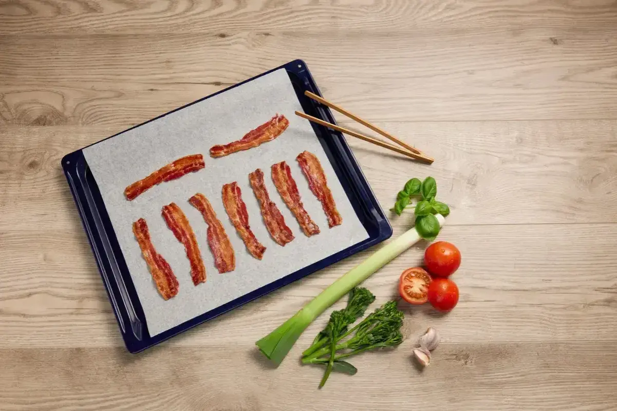 Bacon i ugn på bakplåtspapper, redo att serveras med färska grönsaker.